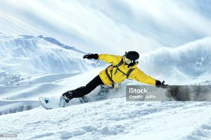 A snowboarder in yellow gear glides down a snowy mountain with stunning peaks.